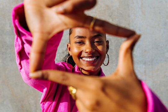 Happy young dancer making finger frame in front of wall