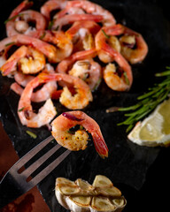 Boiled shrimp on a fork on a dark background.