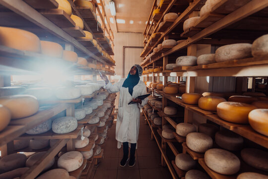 African American Muslim businesswoman checking product quality and entering data into a laptop at a local cheese manufacturing company