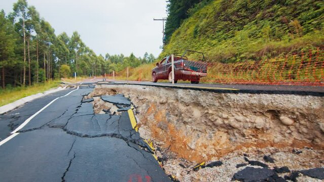 Car moves on the lane of the completely damaged asphalt road in the mountains. Mudflow aftermath, cracked paved road