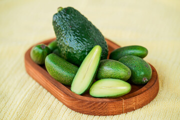 Seedless coctail baby mini avocados whole and half, one avocado in the middle, whole them on the wooden plate, selective focus, closeup