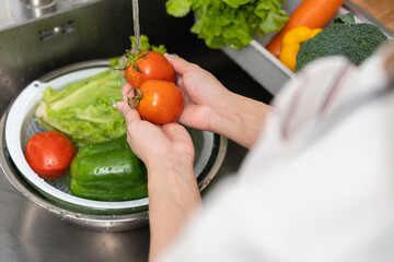 Close up asian young woman washing tomato, broccoli, carrot fresh vegetables, paprika with splash water in basin of water on sink in kitchen, preparing fresh salad, cooking meal. Healthy food people.