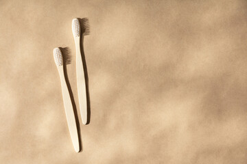 Two natural wooden toothbrushes on natural beige background with leaves shadows, flat lay, top view