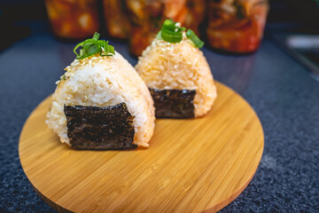 Onigirs filled with kimchi in a wood tray and kimchi in glass jars (kimchi: mix of pickled and fermented vegetables, garlic, chili peppers; onigiri: triangular shaped rice with nori and fill)