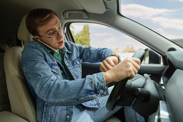 Emotional young man checking time while talking on phone in car. Being late