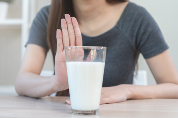 Allergy asian young woman, girl hand in deny, no or push out to avoid for drink milk at home, unhappy and bad stomach ache. Lactose intolerance and dairy food, health problem, belly suffer concept.