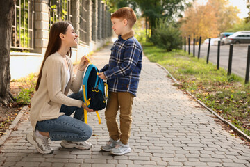Young mom giving school backpack to her son outdoors