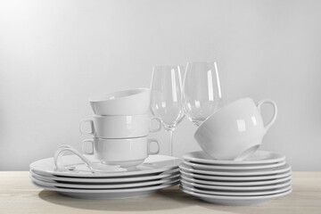 Set of clean dishware and glasses on white wooden table against light background