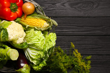 Different fresh vegetables in wicker basket on black wooden table, top view and space for text. Farmer harvesting