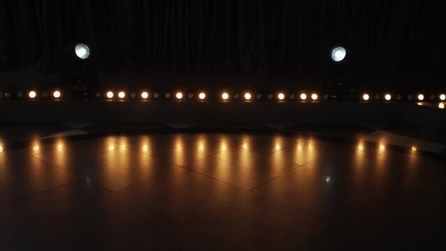Horizontal row of round warm colored halogen lights flashing alternately in romantic setting. On tiled floor in dark hall, rays from lanterns are reflected, forming light music.