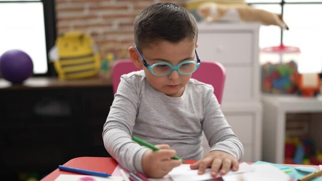 Adorable hispanic toddler student drawing on notebook at kindergarten
