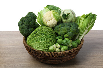 Wicker bowl with different types of fresh cabbage on wooden table against white background
