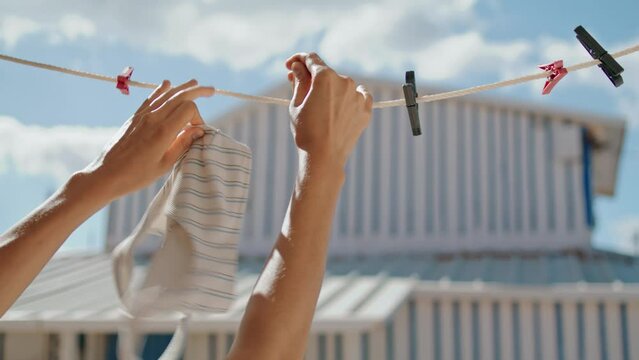 Woman hands taking swimsuit off rope closeup. Striped bikini bra air drying