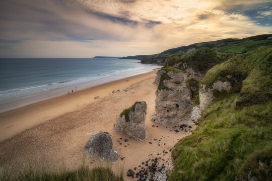 People walking on White Rocks Beach with limestone rock formations at sunset, Causeway Coast, Wild Atlantic Way, County Antrim, Northern Ireland