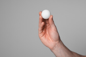 Man with ping pong ball on light grey background, closeup. Space for text