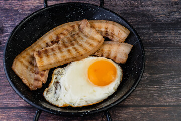 sarten de huevos con panceta encima de una mesa de madera, mujer mojando pan en la yema del huevo