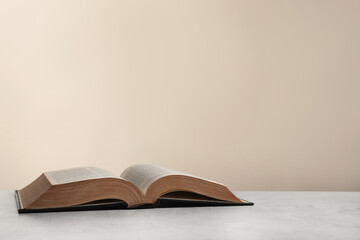 Open hardcover Bible on light grey table, space for text. Religious book