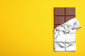 Tasty chocolate bar on yellow background, top view. Space for text