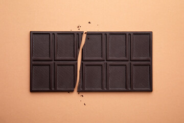 Broken chocolate bar on brown background, top view