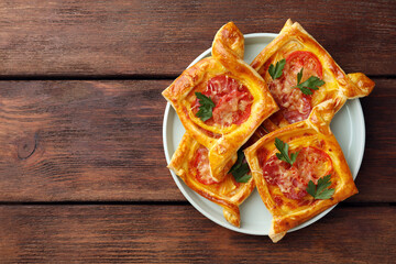 Fresh delicious puff pastry with cheese, tomatoes and parsley on wooden table, top view. Space for text
