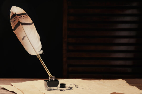 Inkwell with feather pen and vintage parchment with ink stains on wooden table indoors. Space for text