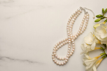 Beautiful pearl necklace and flowers on white marble table, flat lay. Space for text - obrazy, fototapety, plakaty