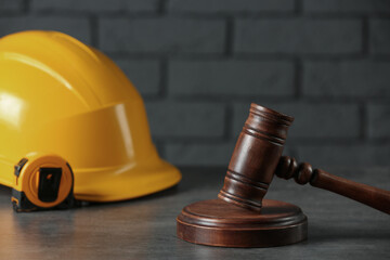 Construction and land law concepts. Judge gavel, protective helmet with tape measure on grey table
