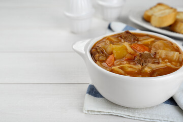 Tasty cabbage soup with meat and carrot on white wooden table, closeup. Space for text