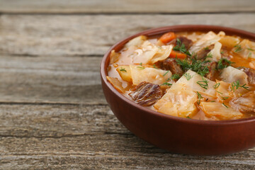 Tasty cabbage soup with meat, carrot and dill on wooden table, closeup. Space for text