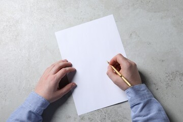 Man writing on sheet of paper with pen at light grey table, top view