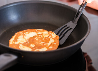 A pancake being flipped by a black spatula in a frying pan.