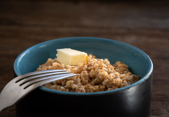 Barley porridge with butter in a ceramic bowl and a fork on a wooden table. Homemade food.