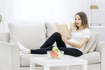 Pregnant woman sitting on sofa and reading a book.