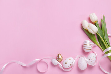 Many painted Easter eggs, tulip flowers and ribbon on pink background, flat lay. Space for text