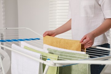 Woman hanging clean terry towels on drying rack indoors, closeup