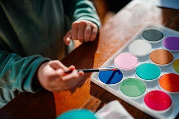 Fototapeta na wymiar A child dips their paintbrush into a fresh pallete of watercolor paints