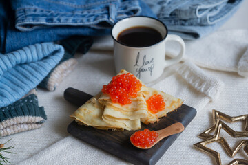 Thin pancakes with red caviar and coffee on the background of warm clothes. Maslenitsa farewell to winter.