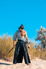 A Japanese warrior in a traditional kimano armed with a katana sword on a sandy shore next to the...