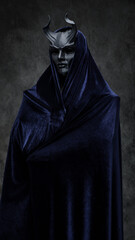 Studio shot of follower of dark cult dressed in dark robe and horned mask.