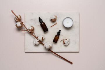 Branch of cotton and beauty products on marble tray. Face care cosmetics, beauty routine