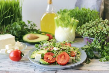 Salad of microgreens, avocado, tomatoes, cheese and arugula, on a plate, against the background of fennel and greens, recipe from natural ingredients, healthy food 