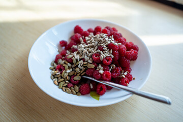 fresh red healthy raspberry with sunflower seed, white plate, wooden background