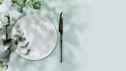 Spring holiday table settings. Empty plate with fork and knife on blue background with eucalyptus leaves. Mockup of romantic summer holiday card with setting suitable for menu. Flat lay, copy space