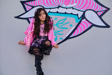 Teenage girl dressed in gothic style posing squatting on graffiti on a skateboarding rink