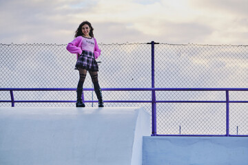 Teenage girl dressed in gothic style sitting and posing in a skate park at sunset