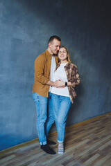 Happy couple in love dressed in shirts, standing on the background of gray wall, looking at empty space, isolated background of gray concrete wall. The concept of a happy couple in love.