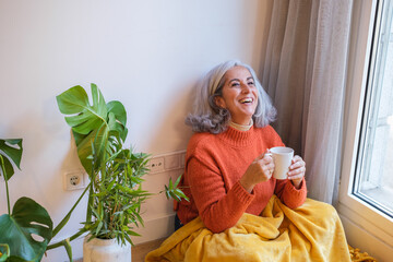 Senior woman with gray hair drinking herbal tea sitting on the floor and relaxing at home. Concept: Lifestyle, senior life, relaxation