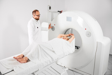 Medical computed tomography or MRI scanner. Male radiologist presses MRI button to examine female...