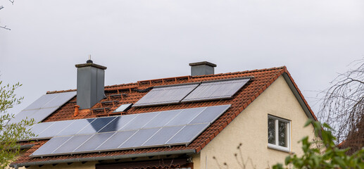 Fototapeta na wymiar View of a house roof with combined photovoltaic systems and solar cells for electricity and hot water in cloudy winter weather