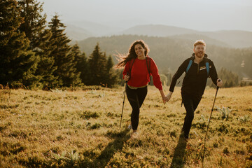 Smiling couple walking with backpacks over green hills